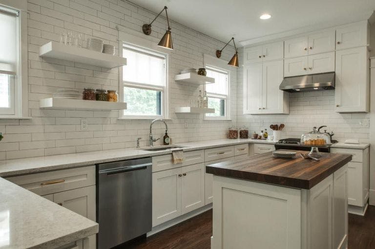 white kitchen with subway tile to ceiling, open shelving, brass swing arm lights over windows and white roller shades