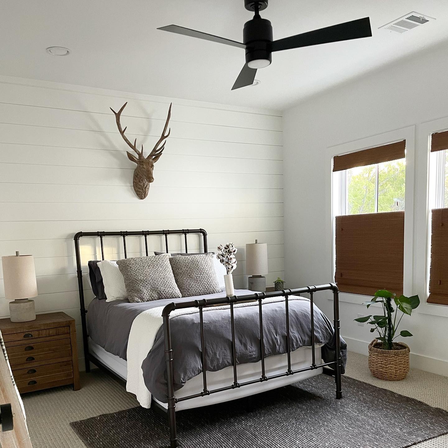 A bedroom decorated for fall with antlers above the bed and dark brown woven wood shades from Blinds.com.