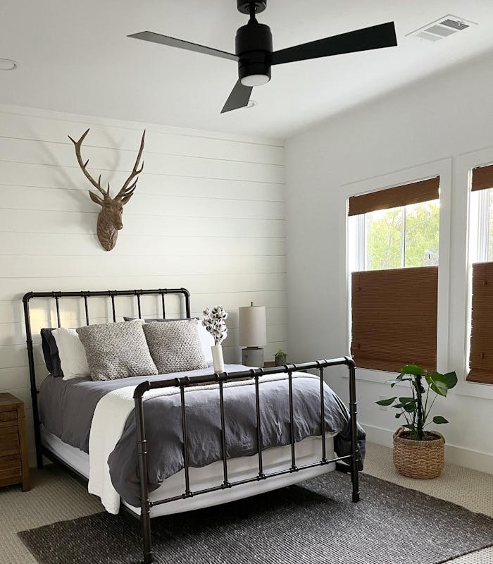 A bedroom decorated for fall with antlers above the bed and dark brown woven wood shades from Blinds.com.