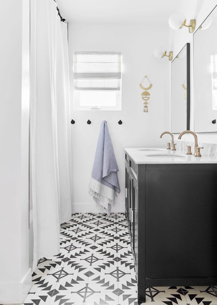 eclectic bathroom with black vanity, patterned tile and small window with white roman shade
