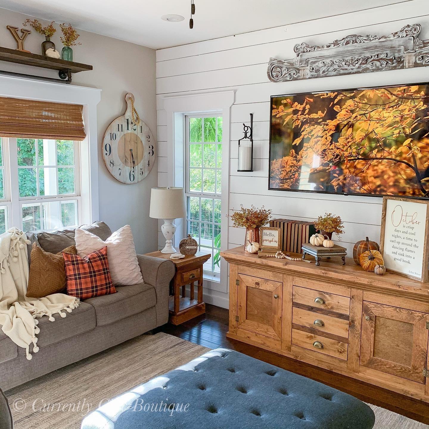 A home decorated for fall with autumn colors. a grey sofa and wooden media console below a frame TV with a beautiful photo of fall leaves.