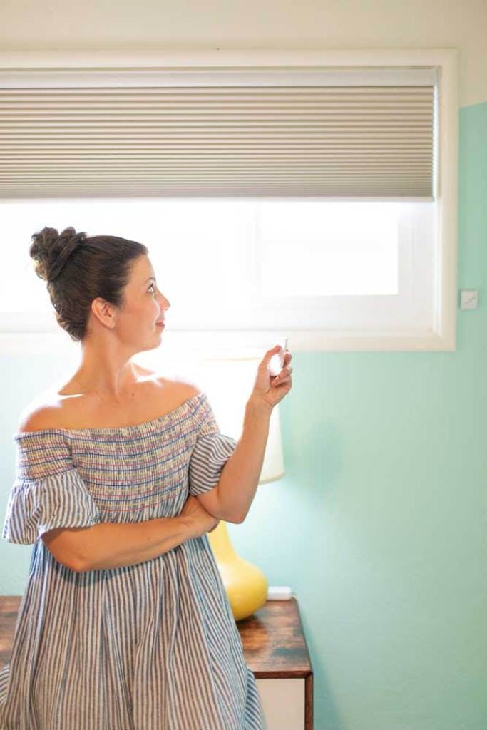 woman opening grey remote controlled window shades in kids bedroom
