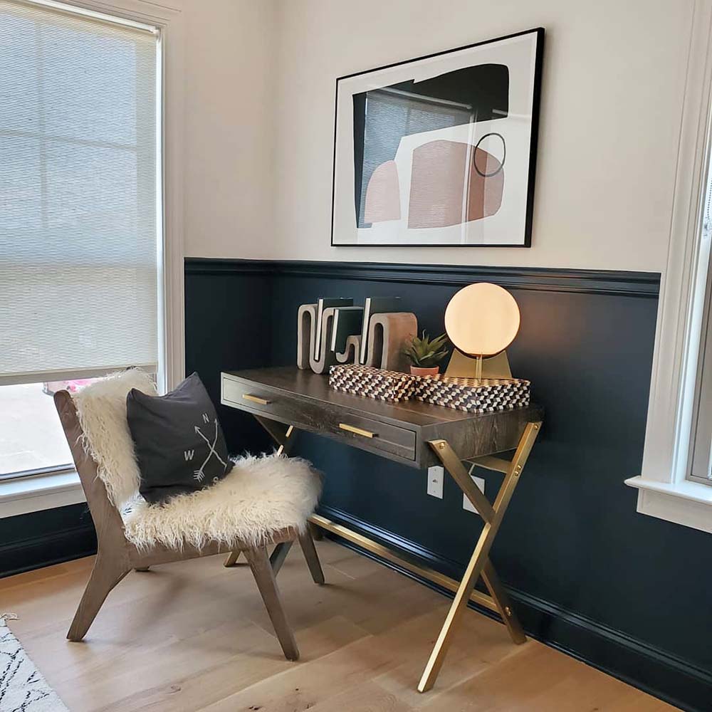 Brass and wood writing desk pushed into a corner near a window with a fluffy, white faux fur chair.