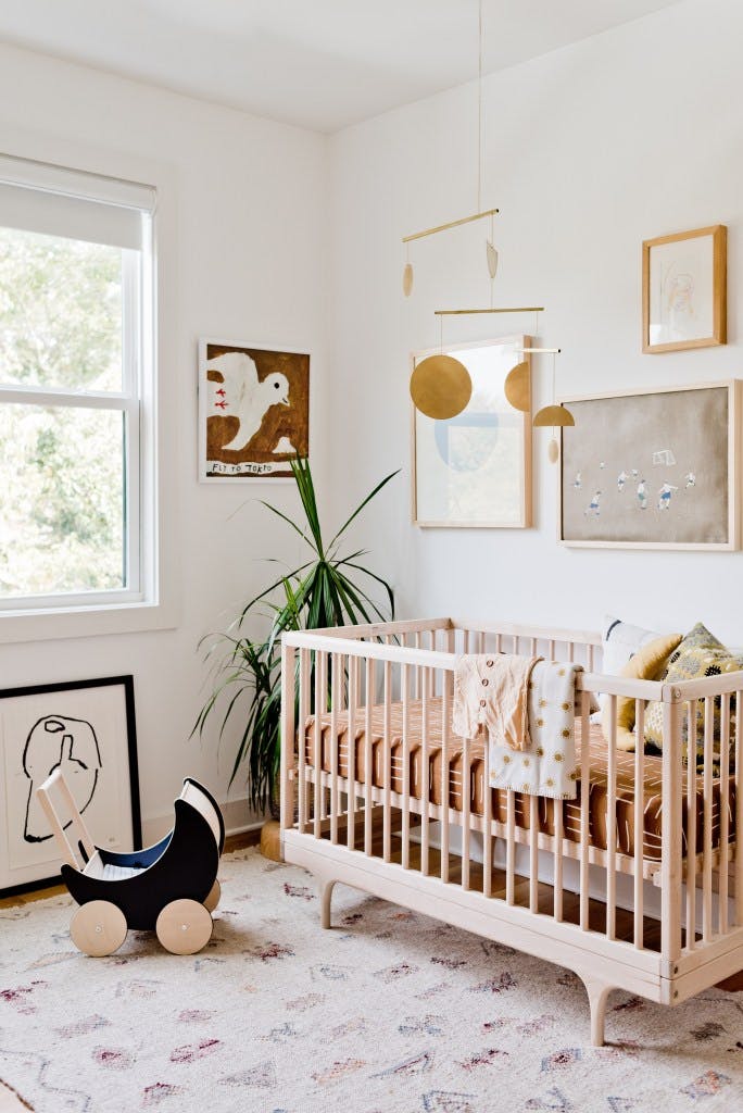 modern nursery with blonde wood crib, brass mobile and white roller shade