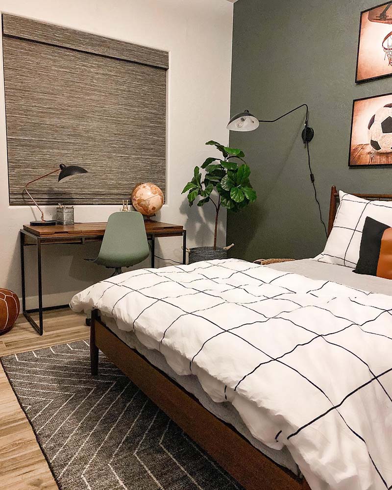 Kids room with sage green wall, white bedding and a woven wood shade over the writing desk.