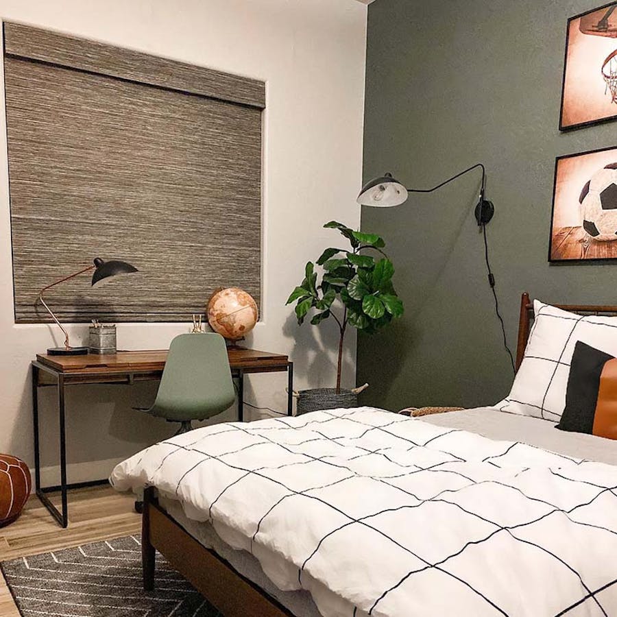 Kids room with sage green wall, white bedding and a woven wood shade over the writing desk.