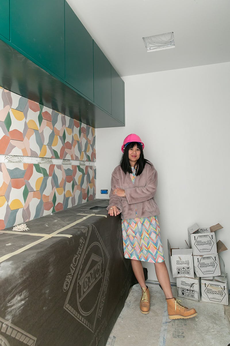 woman standing in laundry room under construction with colorful tile backsplash