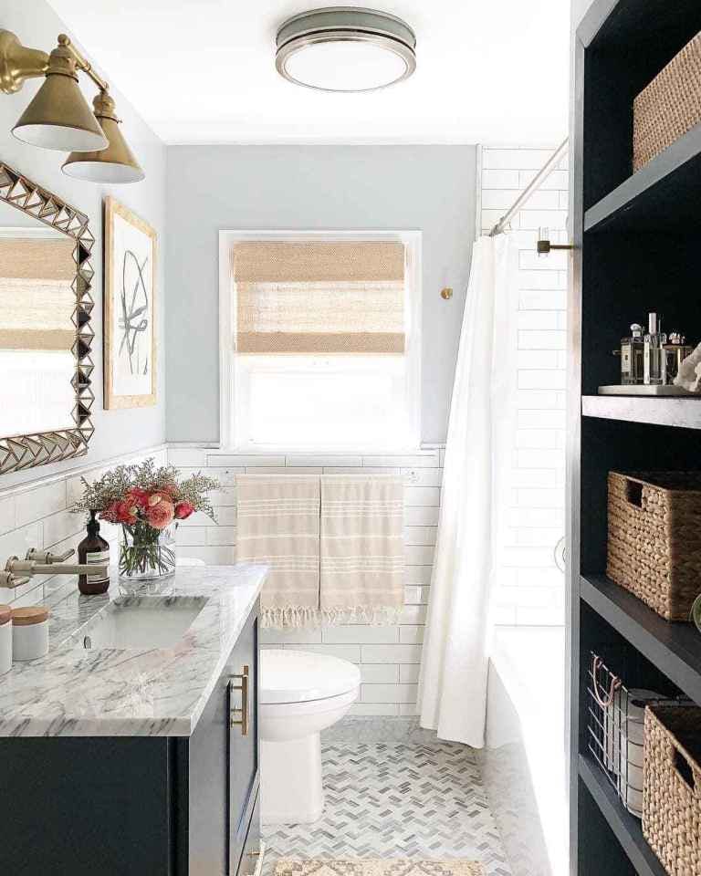 traditional bathroom with herringbone marble floors, marble vanity, brass hardware, light blue walls and tan woven shade over window