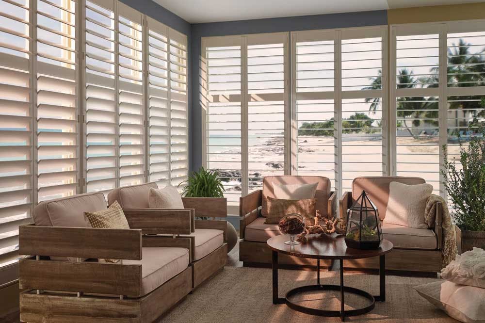 Beachy living room overlooking the water will walls of windows and white Levolor Traditional Shutters installed with slats tilted open.