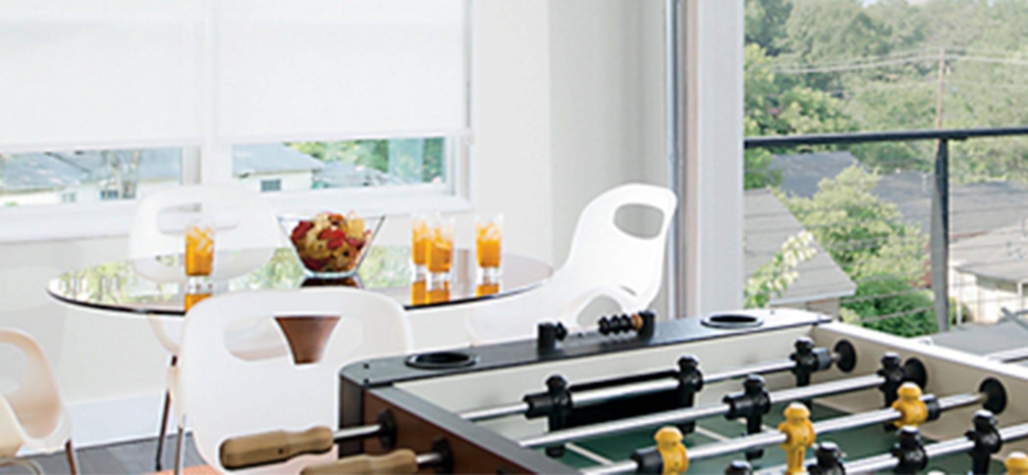 a game room with a foosball table and white solar shades in the background