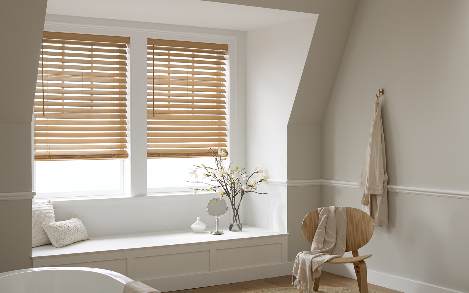 Modern all-white bathroom with light brown faux wood blind window coverings from Blinds.com.
