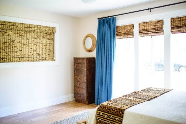 guest bedroom reveal shot with bamboo window shades on short wide window and three smaller windows with blue pinch pleat curtains