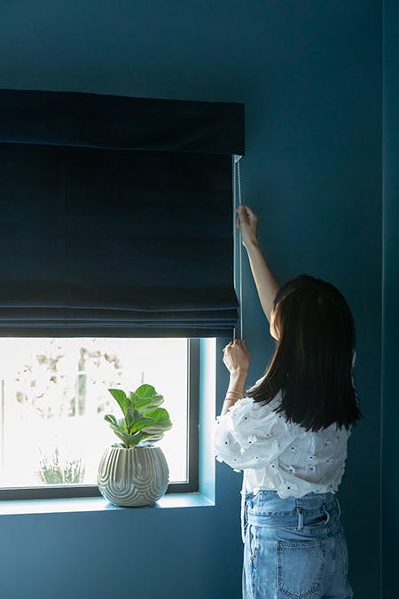 woman opening navy velvet roman shades in dark blue bedroom