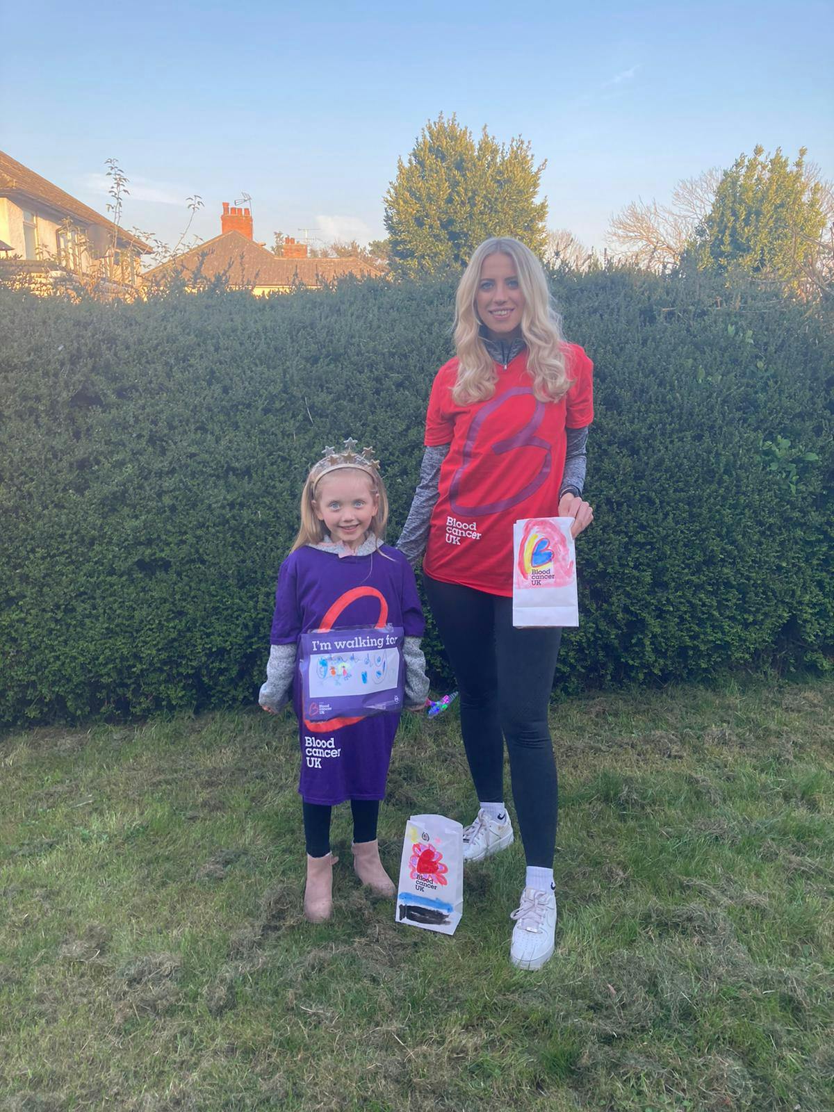 Isla aged 5 and her mum Amy standing outside wearing their Blood Cancer UK t shirts and holding luminary bags with drawings on