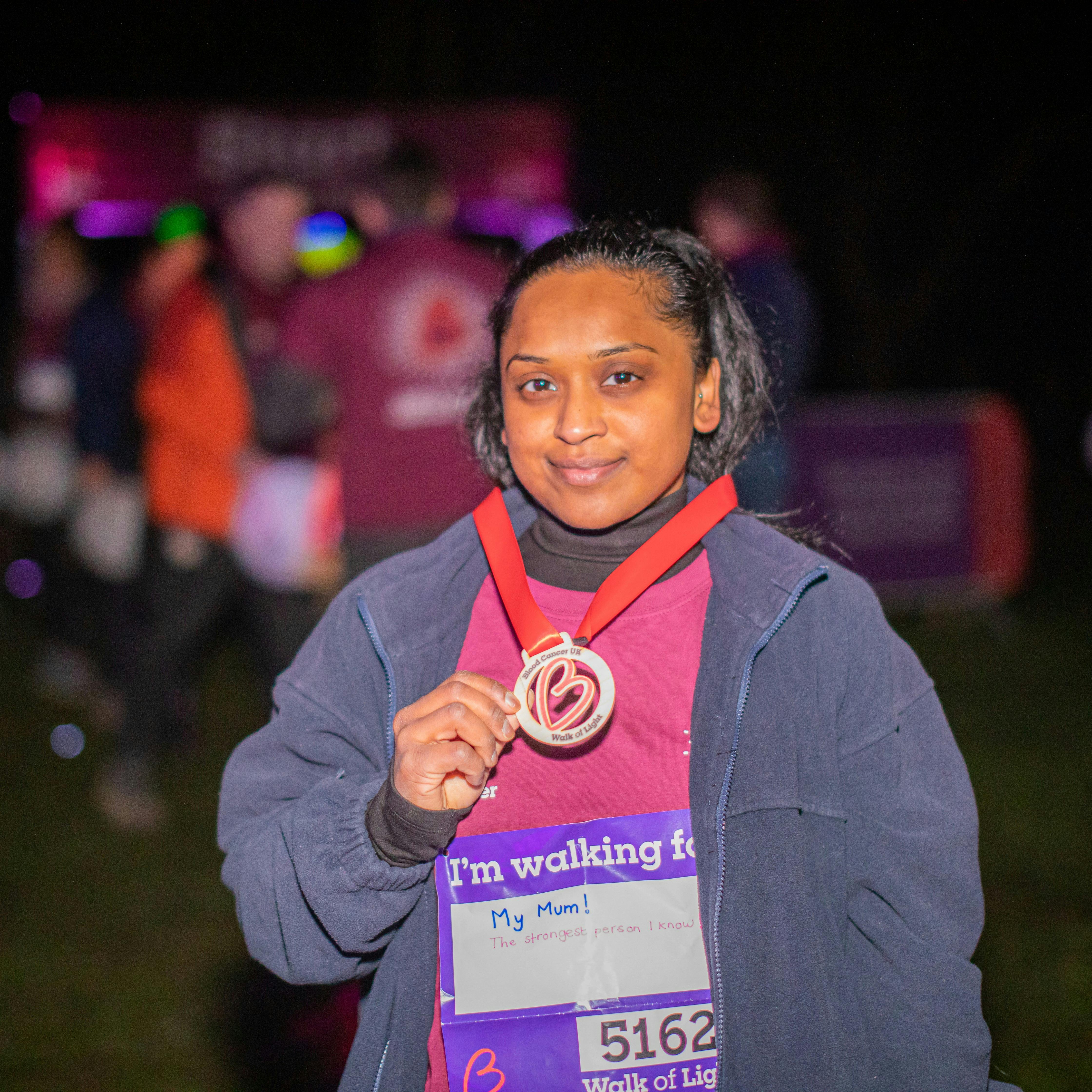 Woman smiling at the camera holding a medal around their neck