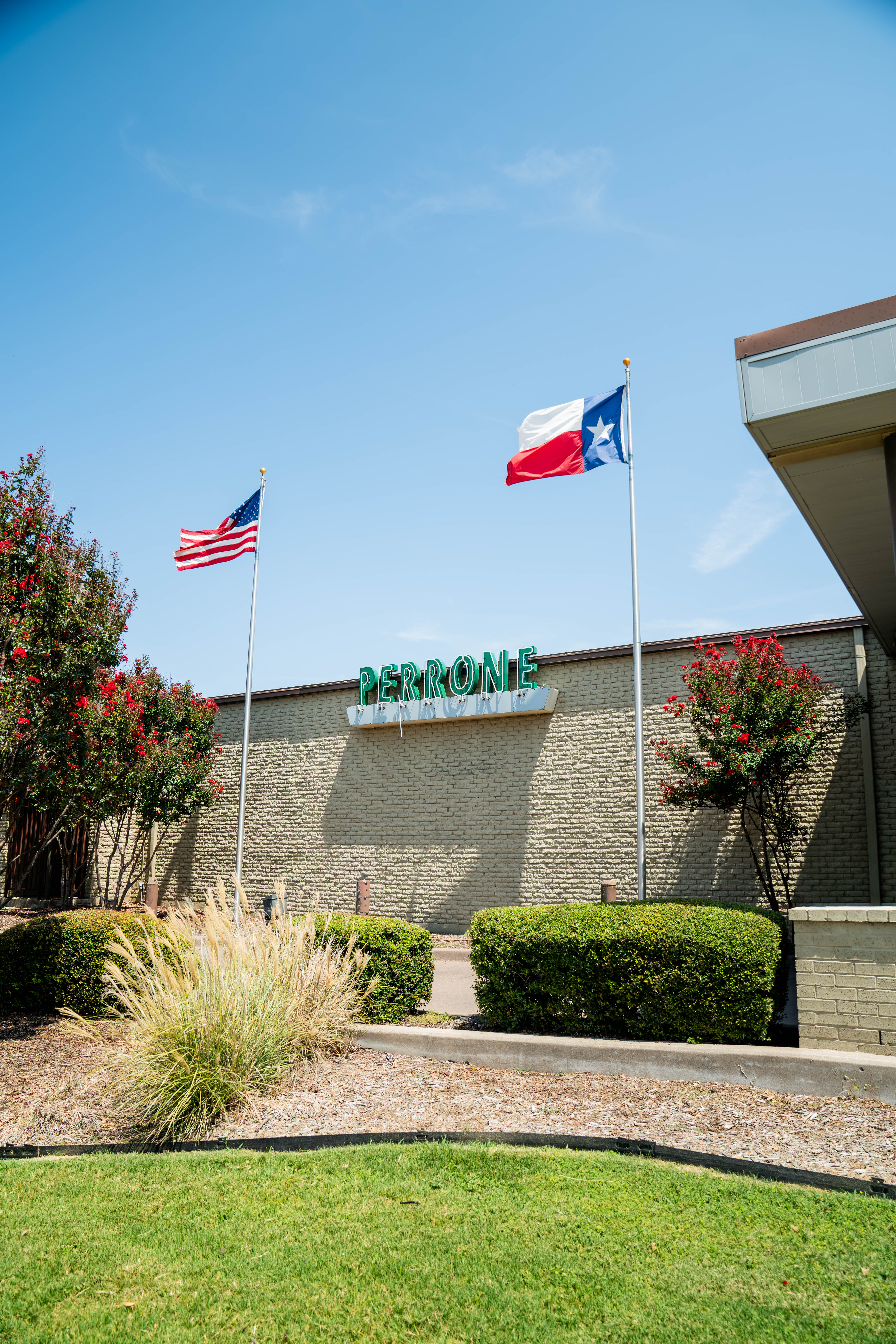Exterior of Perrone Pharmacy on Benbrook Highway in Fort Worth, with American and Texas flags flying over the building.