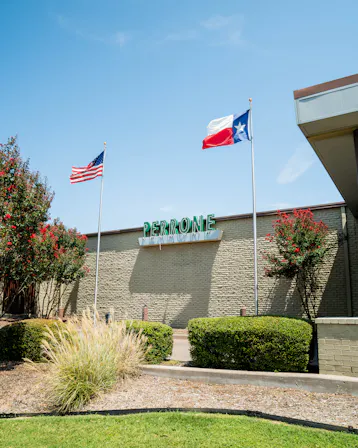 Exterior of Perrone Pharmacy on Benbrook Highway in Fort Worth, with American and Texas flags flying over the building.