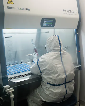 A pharmacist in full protective gear compounding a medication inside a sterile biosafety cabinet.