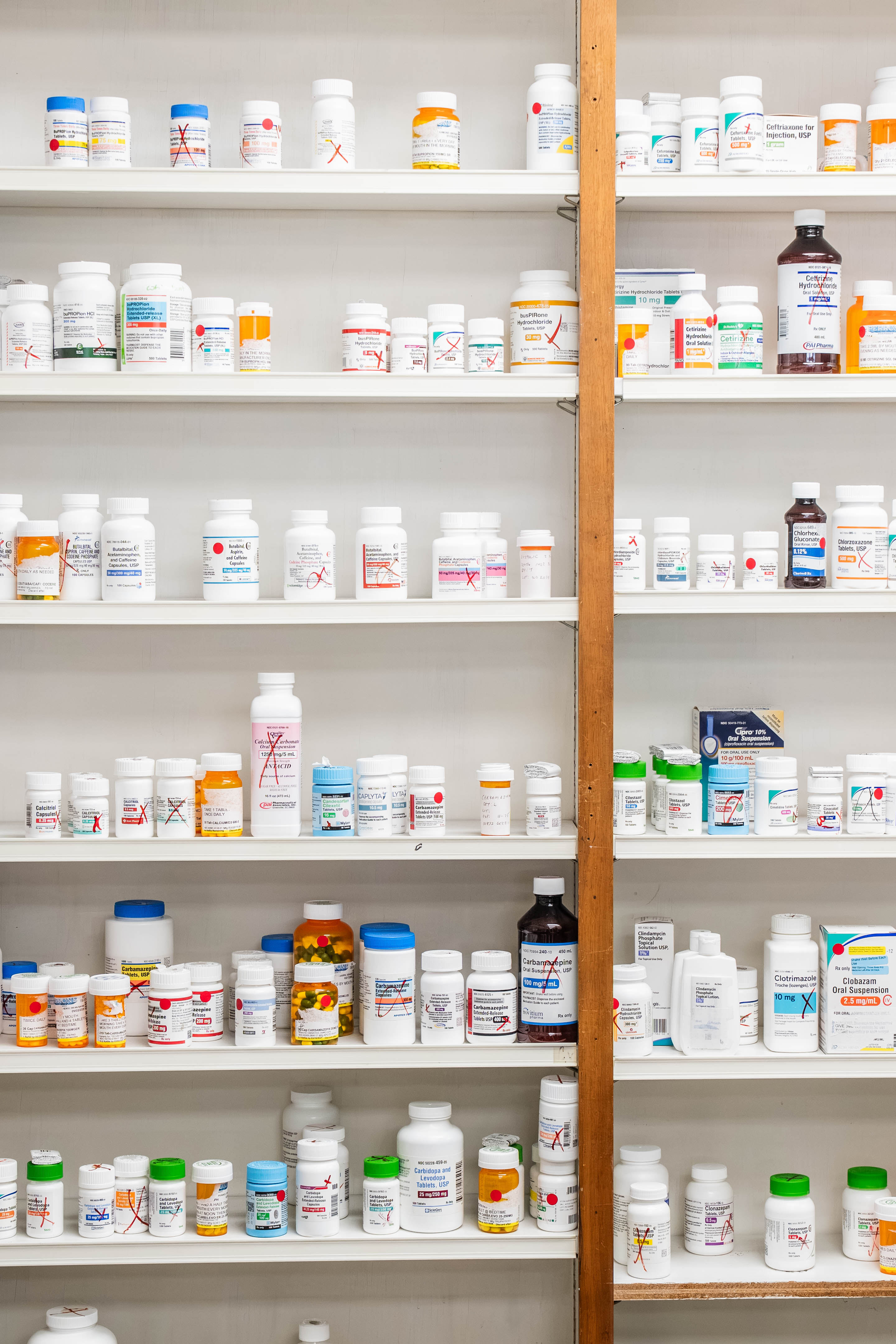 Prescription medication bottles lined up on white pharmacy shelves.