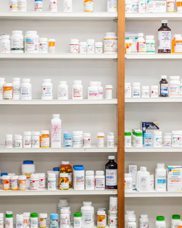 Prescription medication bottles lined up on white pharmacy shelves.