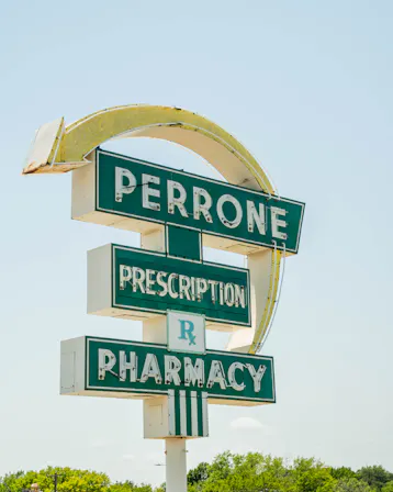 Perrone Pharmacy’s vintage green and white roadside sign reading “Perrone Prescription Pharmacy.”