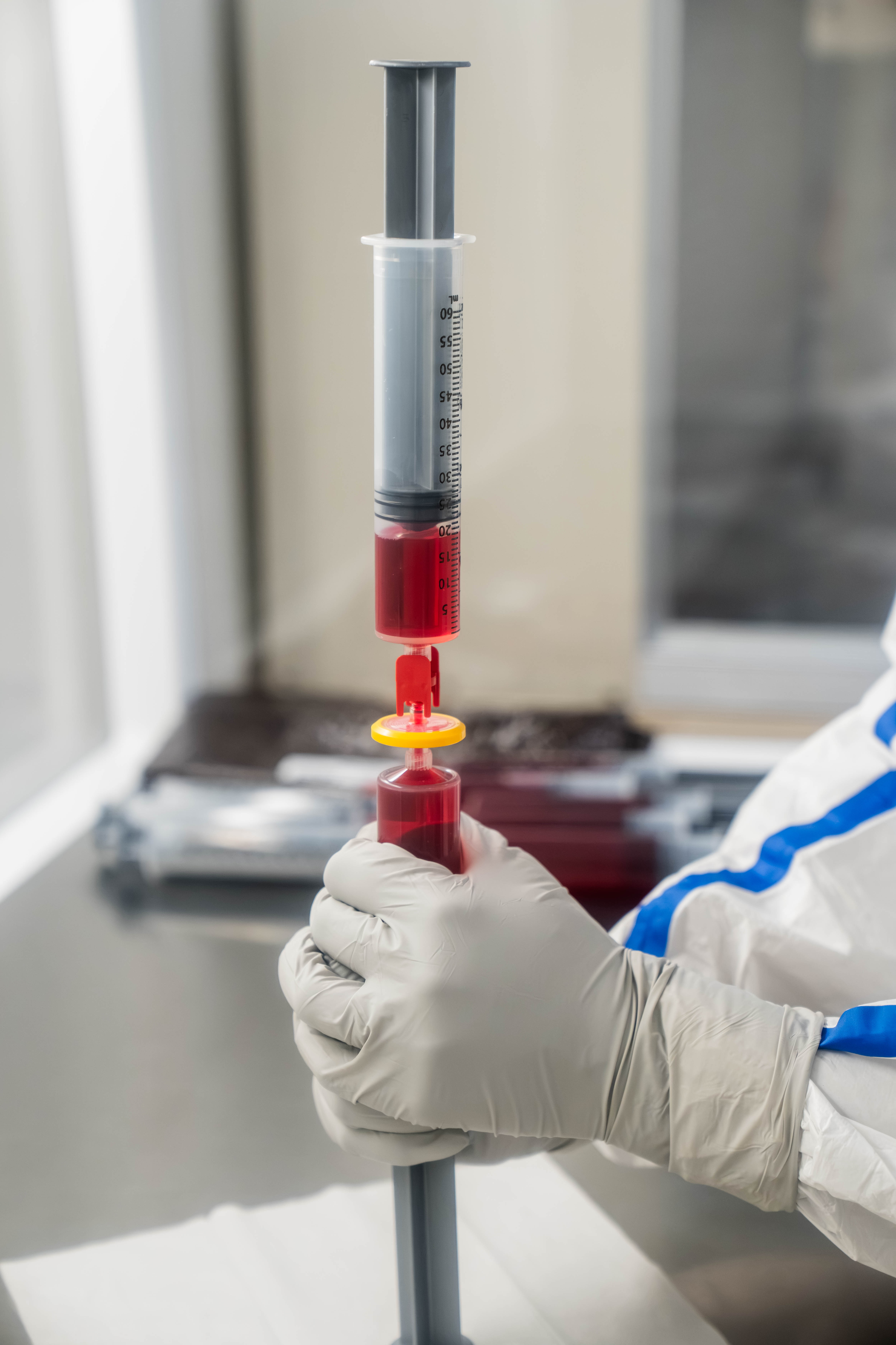 A gloved pharmacist holding a syringe while preparing a compounded medication.
