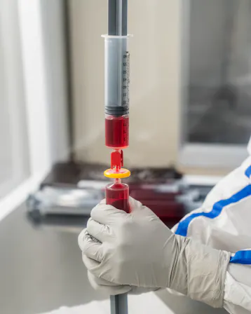 A gloved pharmacist holding a syringe while preparing a compounded medication.