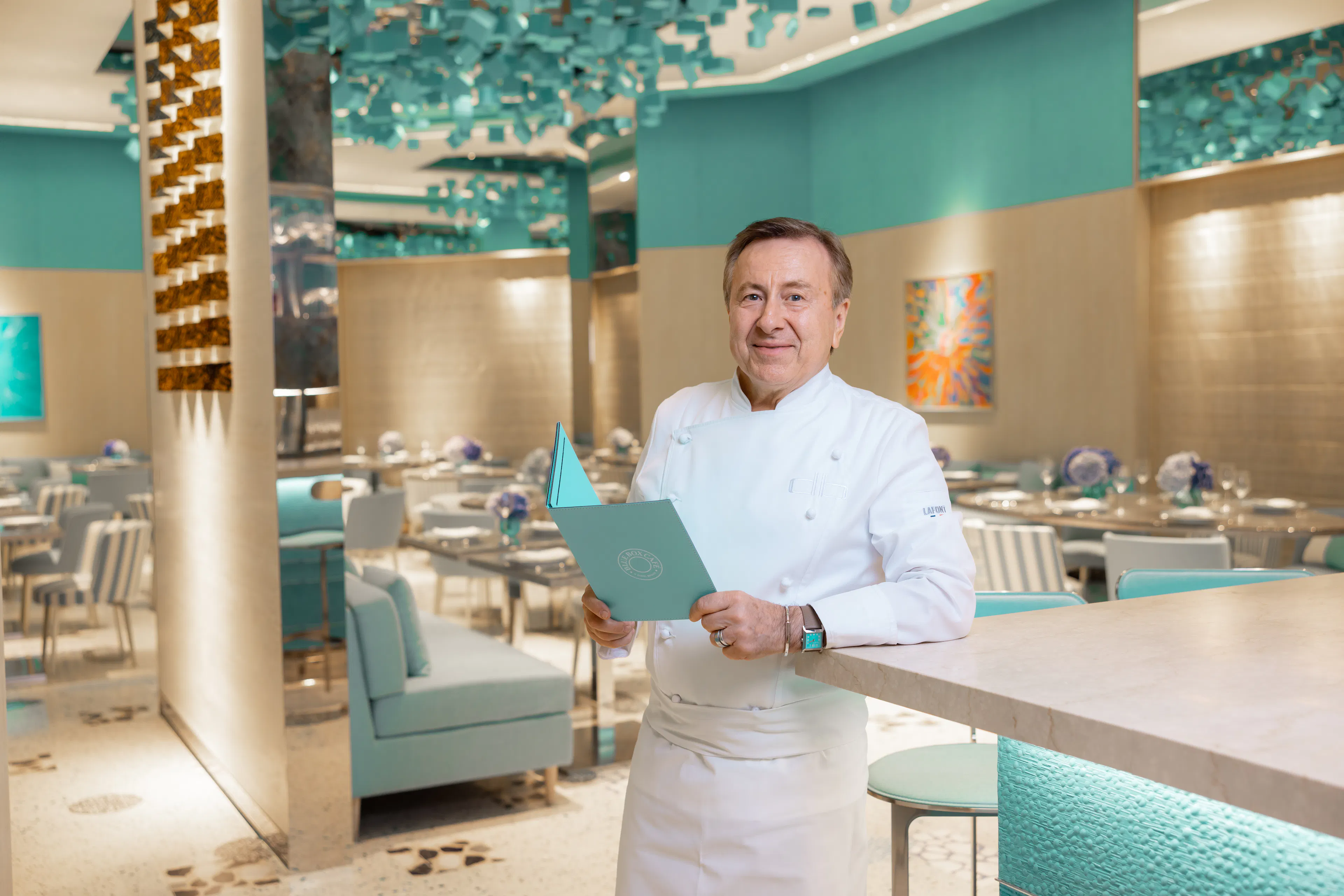 Chef Daniel Boulud at Blue Box Café at Tiffany & Co. South Coast Plaza, holding a signature Tiffany Blue menu inside the elegant restaurant.