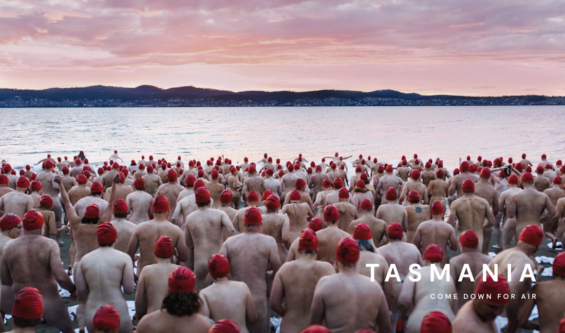 An image of a large group of people in red swimming caps, wading into a serene lake at sunrise to go skinny dipping. Tasmania, come down for air.