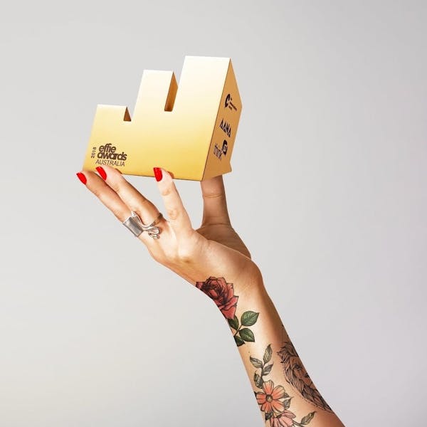 An image of a tattooed hand holding up a small, geometric trophy.