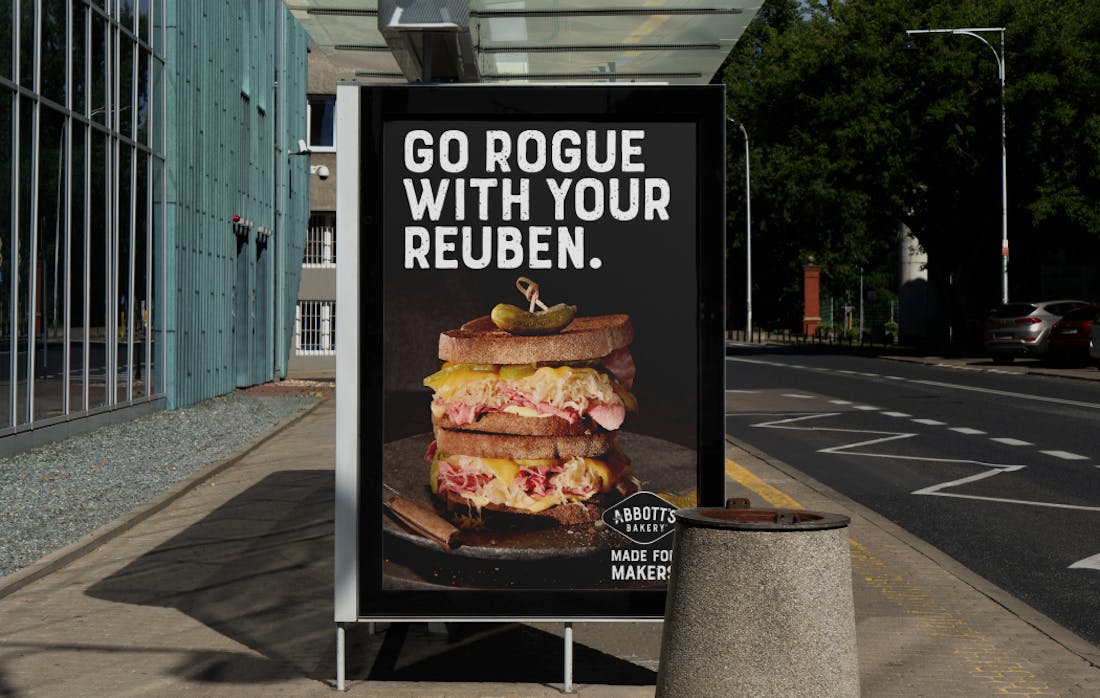 A bus stop advertisement for Abbott's Bakery showcasing an appetising image of a toasted ham sandwich on a black plate. A headline reads: "Go rogue with your reuben".