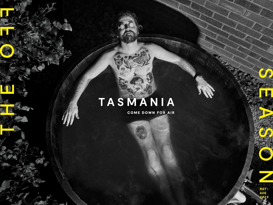 An ad for Tourism Tasmania featuring a black and white image of a tattooed man floating in a small pool. The tagline reads: "The off season".