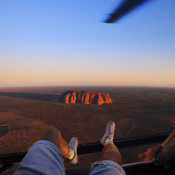 An image of a person in a helicopter gazing at Uluru, a sacred rock formation in the Australian outback.