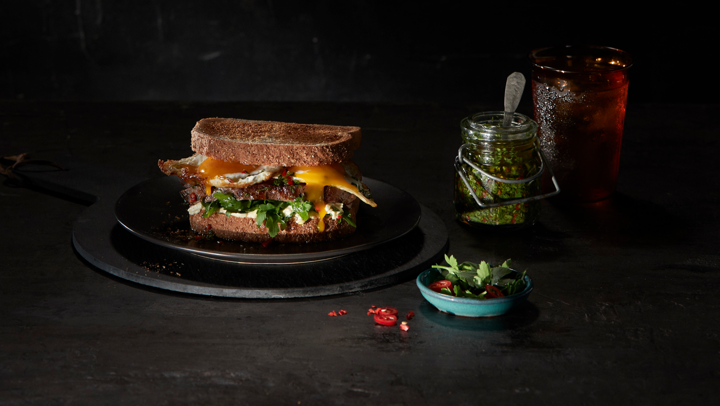 An appetising image of a toasted sandwich on a black plate, accompanied by a small dish of garnishes.