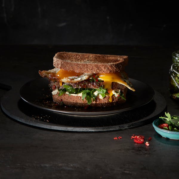 An appetising image of a toasted sandwich on a black plate, accompanied by a small dish of garnishes.