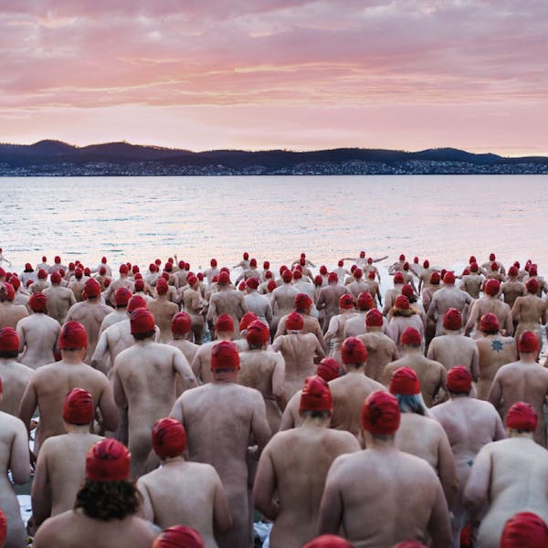 An image of a large group of people in red swimming caps, wading into a serene lake at sunrise to go skinny dipping.