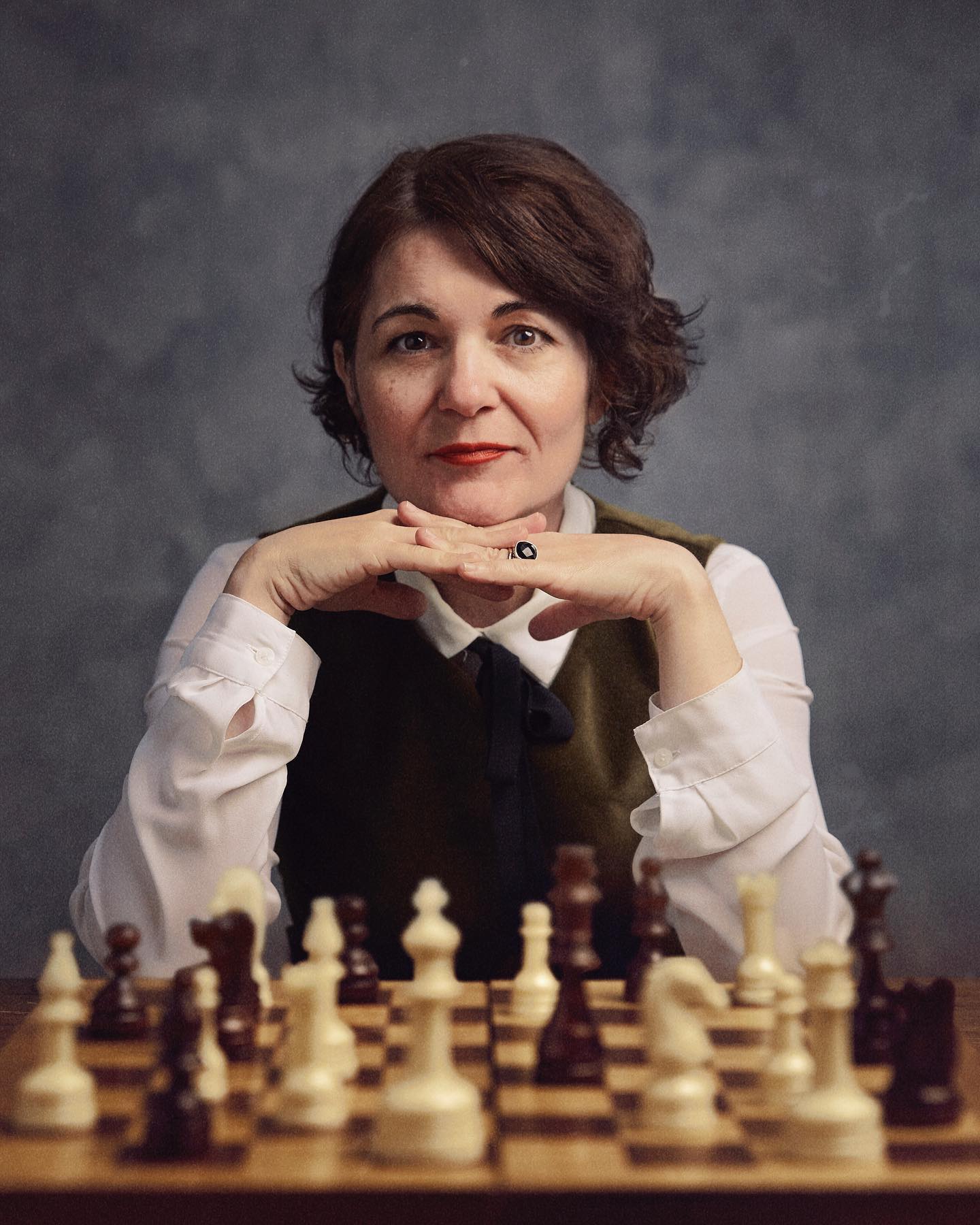 An image of a woman with a pensive expression sitting behind a chess table.