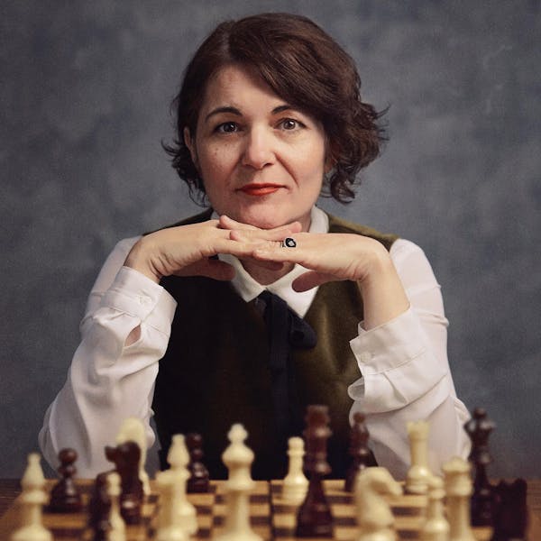 An image of a woman with a pensive expression sitting behind a chess table.