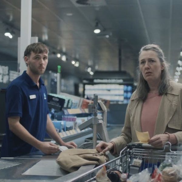 An image of a woman being served by a man at a supermarket checkout.