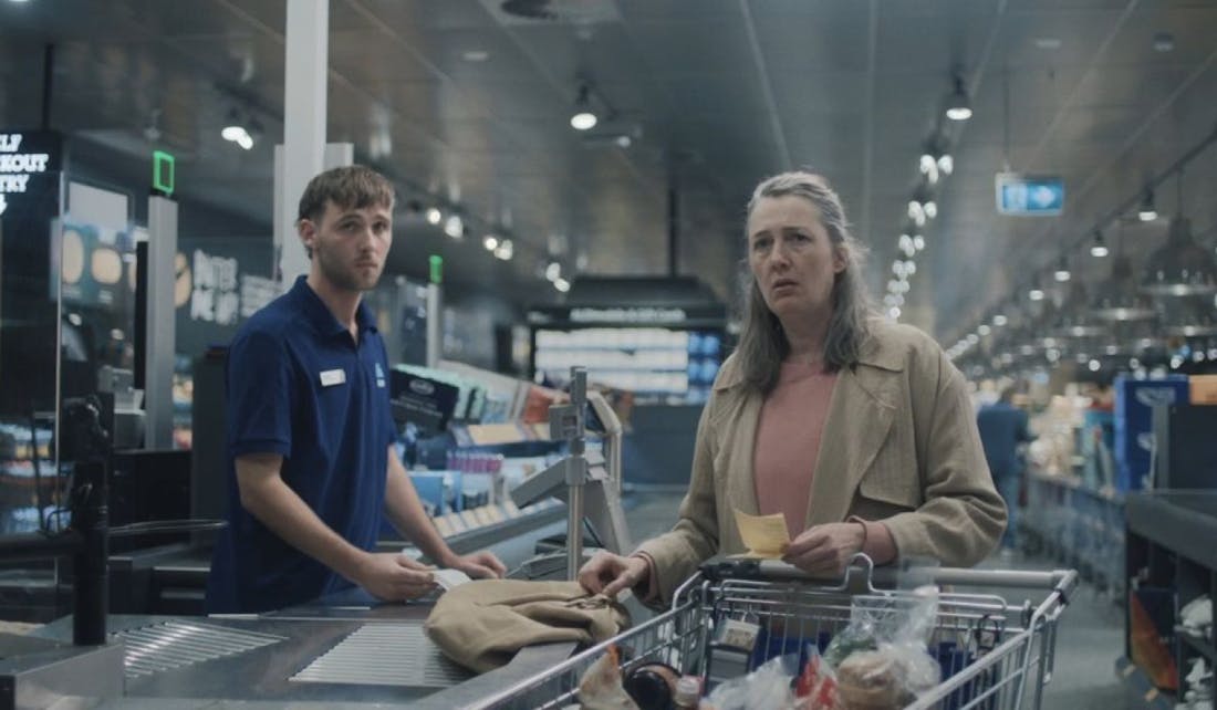 An image of a woman being served by a man at a supermarket checkout.