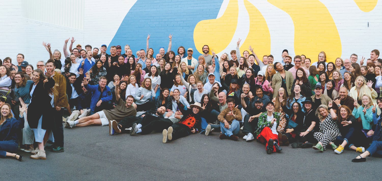 An image of a large group of cheerful people standing in front of a colourful wall.