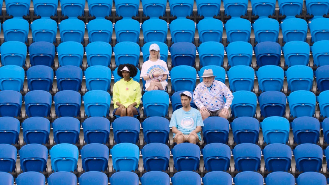 four people in colourful AO merchandise sitting in the stands of a tennis court.