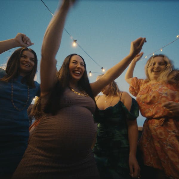 A pregnant woman dancing with her friends, a focus on her stomach.