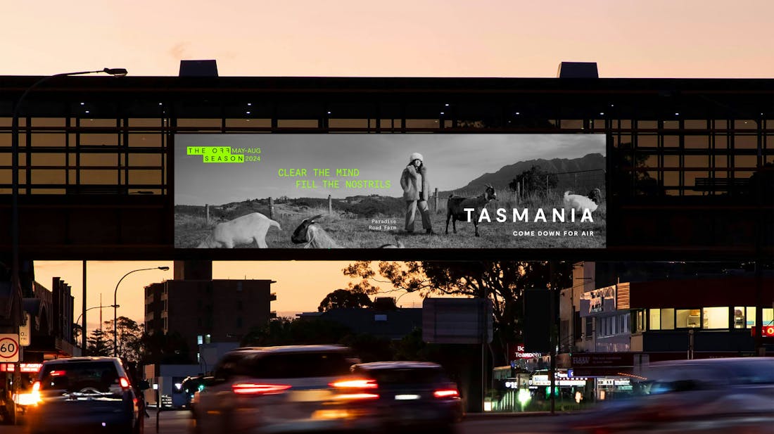Black and white billboard of woman in a field of goats with green text reading 'The Off Season May-Aug 2024, Clear the Mind Fill the Nostrils, Tasmania Come Down For Air'
