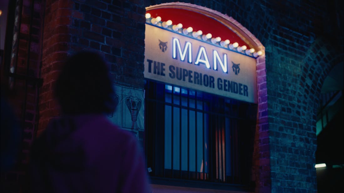 A young boy looking up at a sign saying 'Man: The Superior Gender'