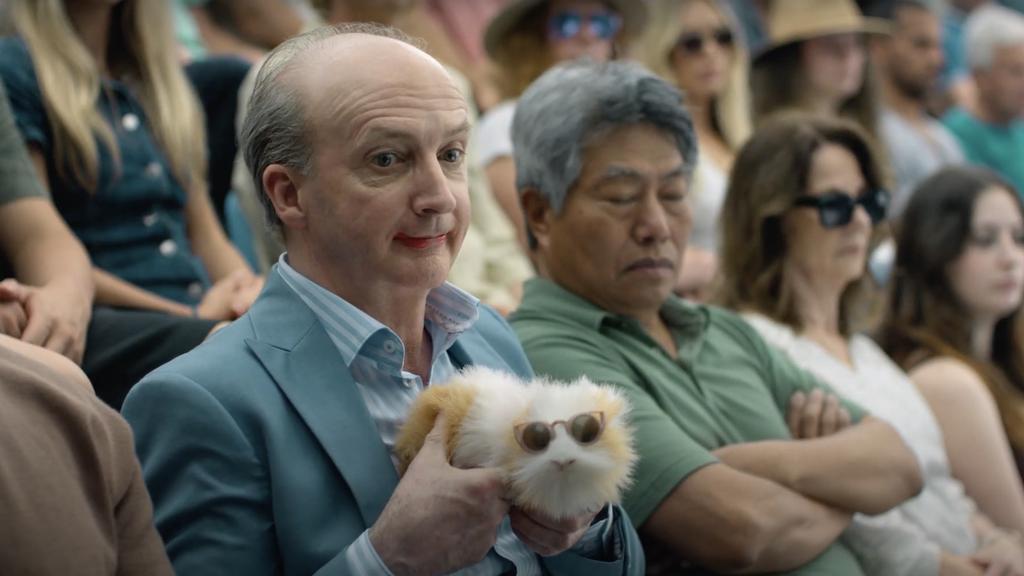 A man watching a tennis game holding a guinea pig 