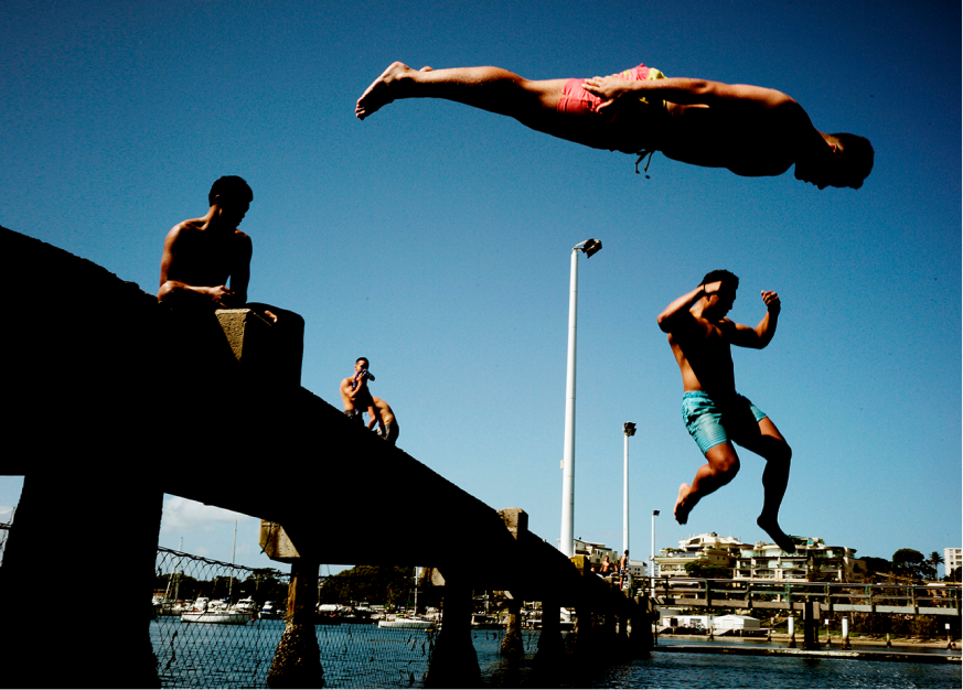 An image of a group of young men diving into water from a jetty. 