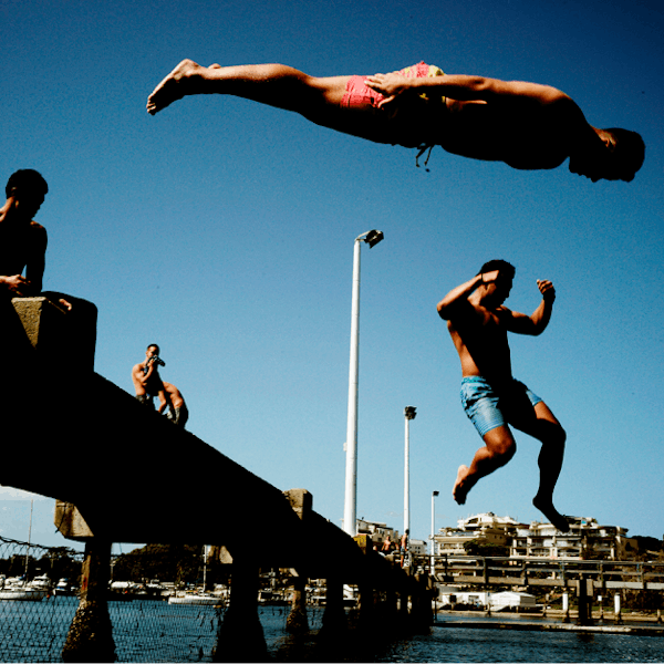 An image of a group of young men diving into water from a jetty. 