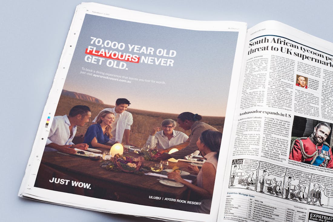 Newspaper advertisement showing people dining at a restaurant with Uluru in the background.