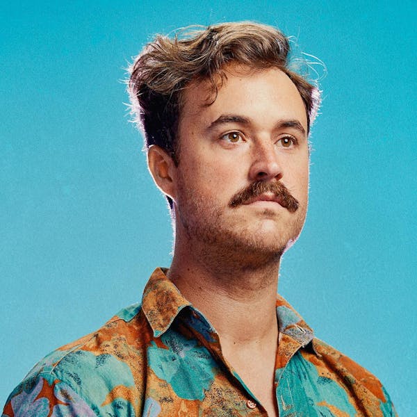 A portrait of a man with short hair, a moustache, and a vibrant floral shirt.